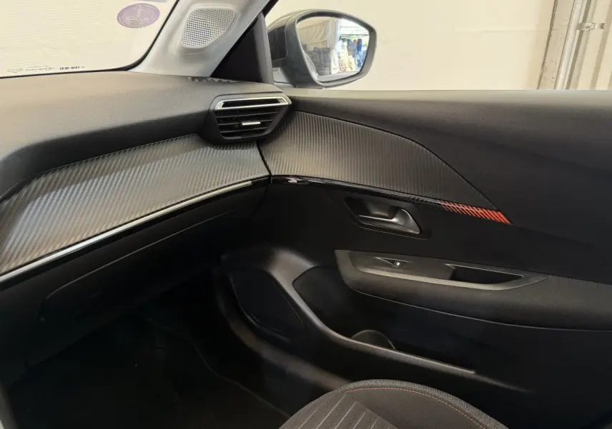 Intérieur côté passager de la Peugeot 208 noire, avec garniture carbone et détail rouge sur la porte.