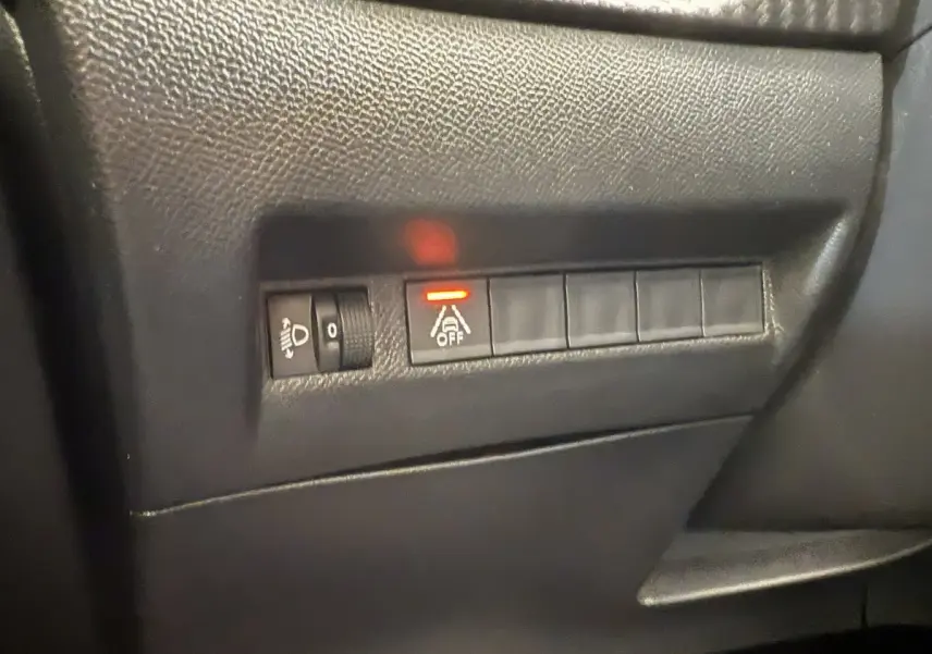 Gros plan sur les commandes de réglage des phares et désactivation de l'assistance au maintien de voie dans une Peugeot 208 noire 2021.