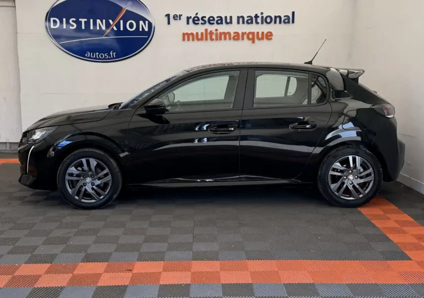 Profil côté gauche d'une Peugeot 208 noire 2021 garée en intérieur sur sol damier gris et orange.