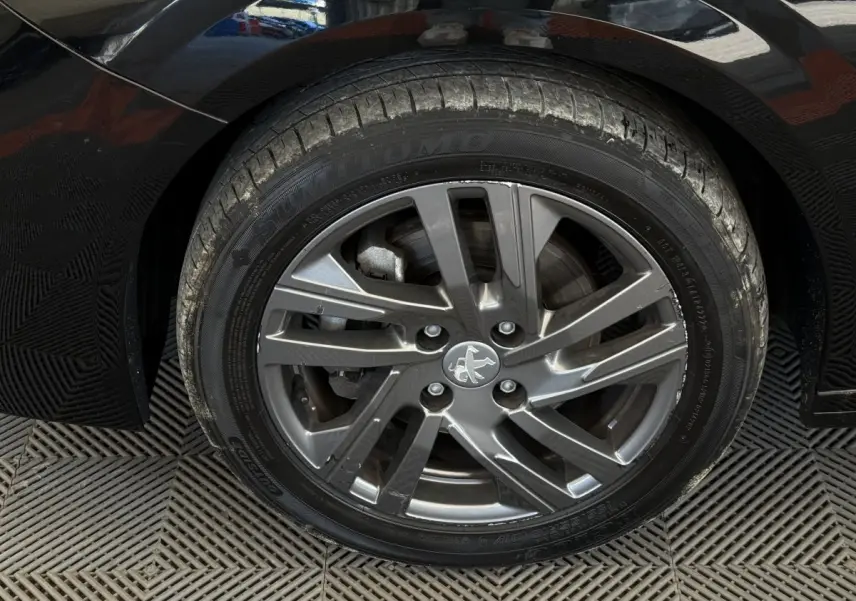 Gros plan sur la roue avant droite noire d'une Peugeot 208 2021 avec jante alliage gris foncé et logo lion central.