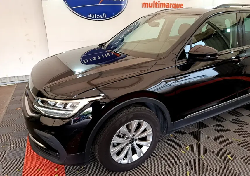 Vue 3/4 avant gauche d'un Volkswagen Tiguan noir brillant avec jantes alliage et phares LED allumés.