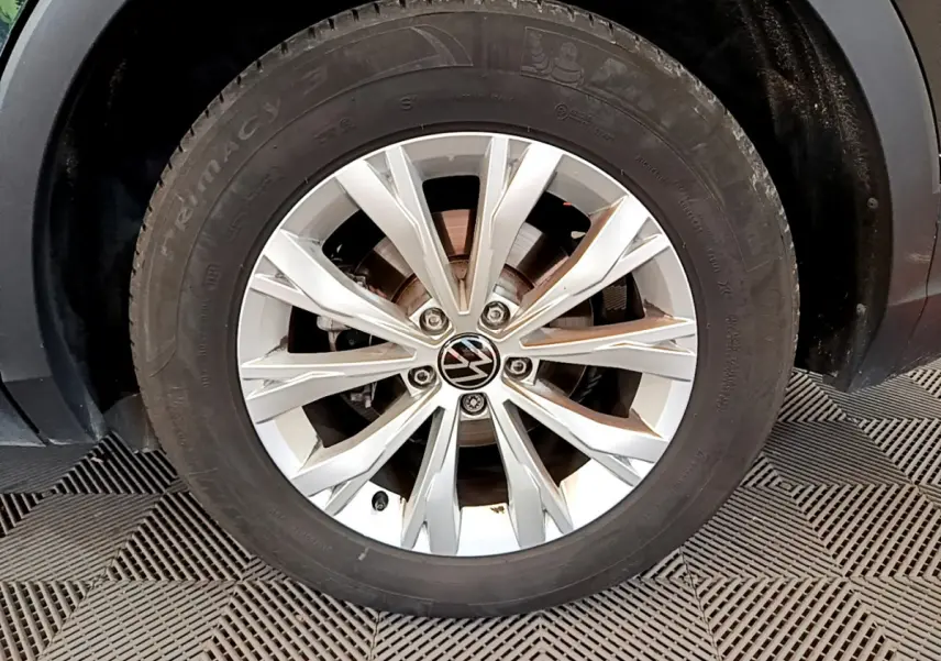 Gros plan sur la roue avant droite du Volkswagen Tiguan noir, mettant en valeur la jante alliage argentée et le logo VW.