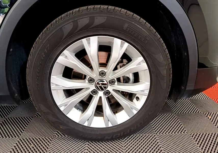 Gros plan sur la roue avant gauche du Volkswagen Tiguan noir, jante alliage argentée avec logo VW central.