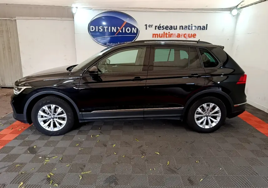 Profil côté gauche d'un Volkswagen Tiguan noir 2021 garé en intérieur avec jantes alliage et barres de toit noires.