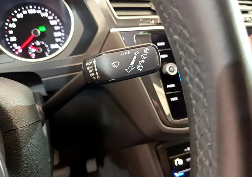 Gros plan sur la commande d’essuie-glace à gauche du volant cuir du Volkswagen Tiguan noir, tableau de bord en arrière-plan.