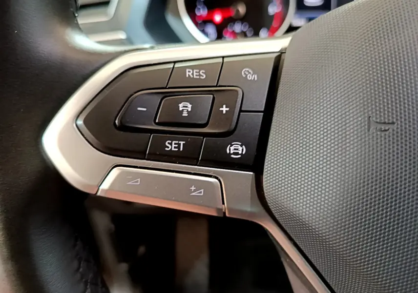 Gros plan sur les commandes du volant côté gauche du Volkswagen Tiguan noir, mettant en avant les boutons de régulateur de vitesse.