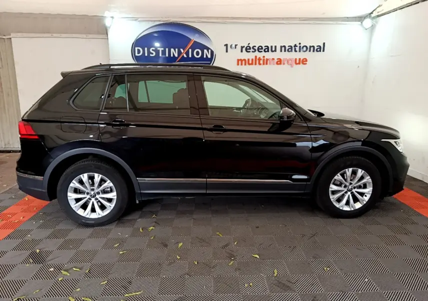 Profil côté gauche d'un Volkswagen Tiguan noir 2021 garé en intérieur avec jantes alliage et barres de toit noires.