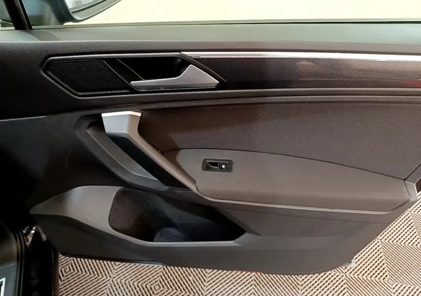 Intérieur côté gauche de la porte avant noire du Volkswagen Tiguan 2021 avec poignée argentée et panneau de commande verrouillage.