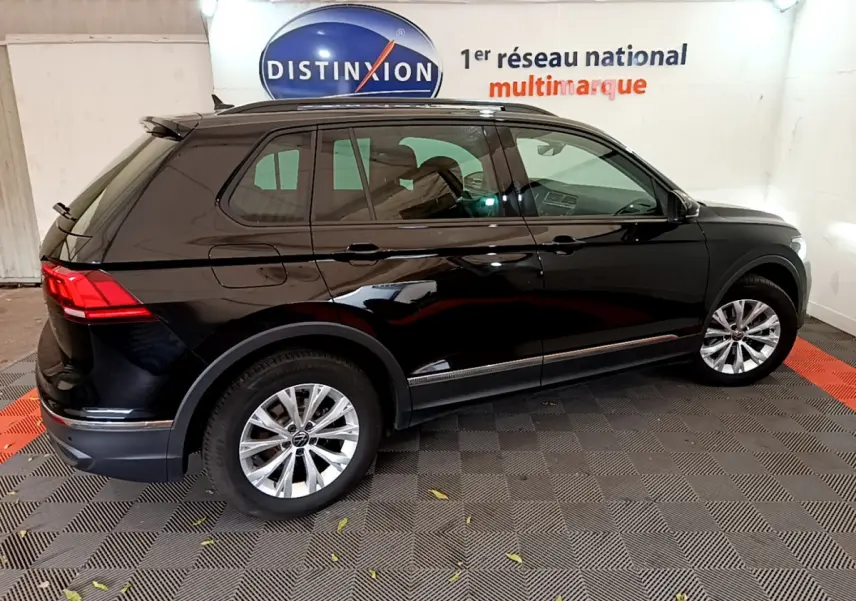 Vue latérale côté droit d'un Volkswagen Tiguan noir 2021 garé en intérieur avec jantes argentées et toit noir.