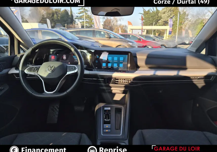Vue intérieure avant de la Volkswagen Golf 2023, tableau de bord noir avec écran tactile central et volant cuir multifonctions.