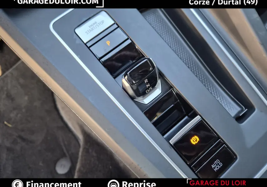 Gros plan sur la console centrale de la Volkswagen Golf 2023, montrant le levier de vitesses automatique et le bouton de frein à main électronique.