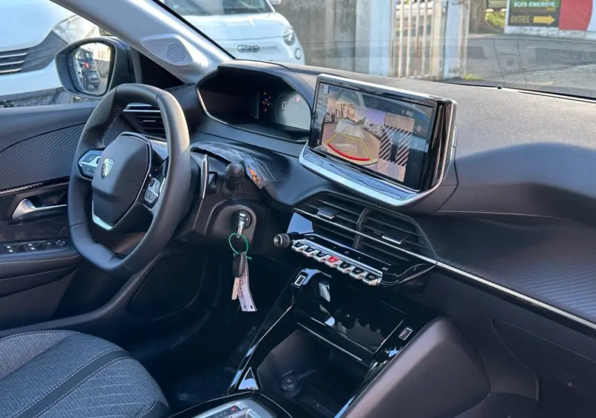 Vue intérieure côté conducteur du Peugeot 208 blanc 2025, avec écran tactile affichant la caméra de recul et volant multifonction.
