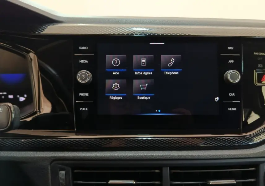 Écran tactile central du tableau de bord du Volkswagen Taigo gris foncé, affichant le menu principal avec options d’aide et téléphone.