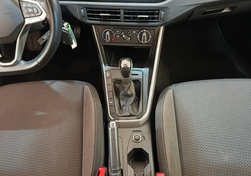 Vue intérieure centrée sur la console centrale et tableau de bord du Volkswagen Taigo gris foncé avec écran tactile et levier de boîte auto.