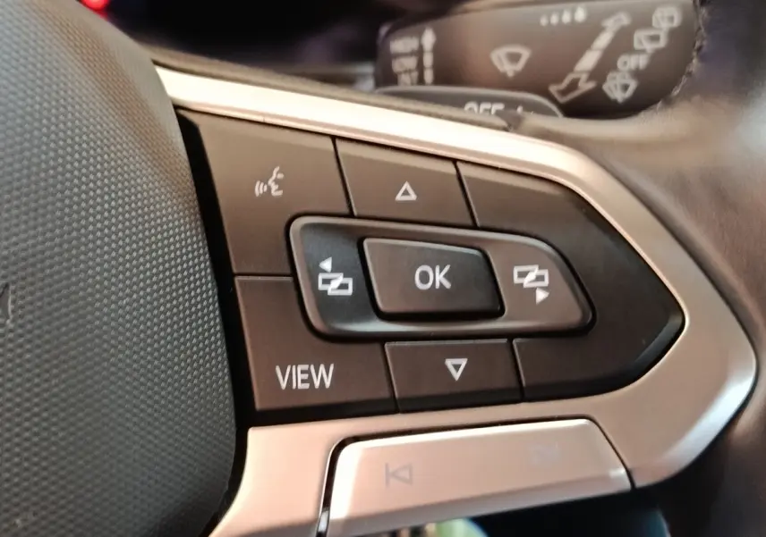 Gros plan sur les commandes multifonctions à gauche du volant du Volkswagen Taigo gris foncé, avec boutons noirs et cadre argenté.