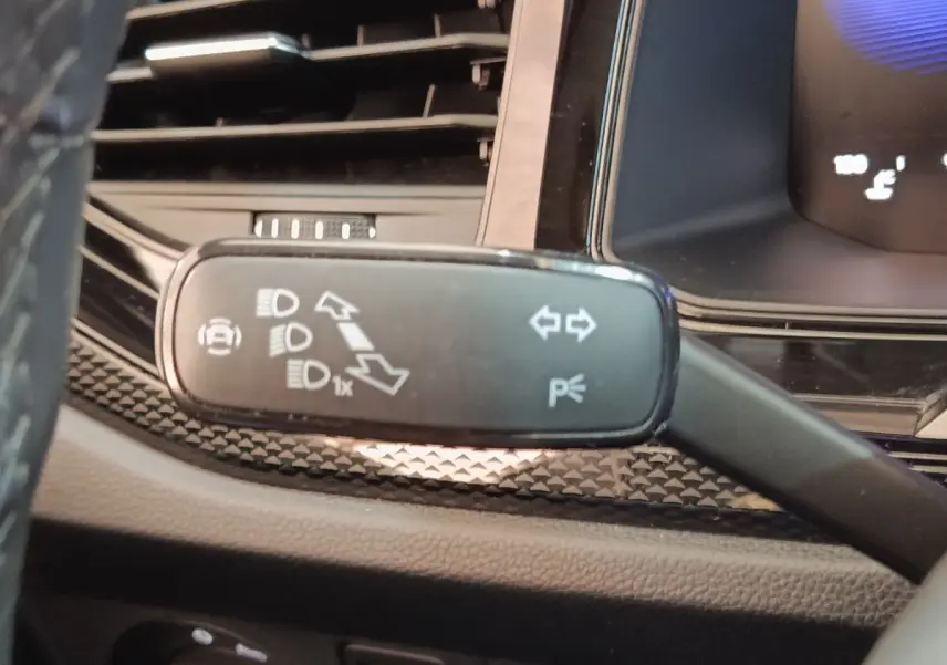 Gros plan sur la commande de clignotants et feux, tableau de bord partiellement visible du Volkswagen Taigo gris foncé.