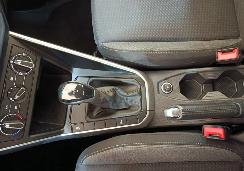 Vue intérieure centrée sur la console centrale du Volkswagen Taigo gris foncé avec levier de vitesse automatique et frein à main.