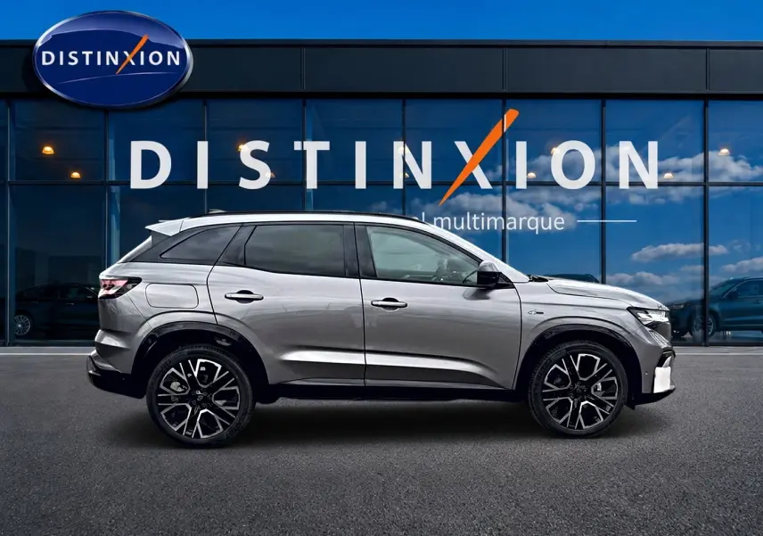 Profil droit du Renault Austral gris schiste avec jantes alu noires, devant une vitrine bleue Distinxion multimarque.