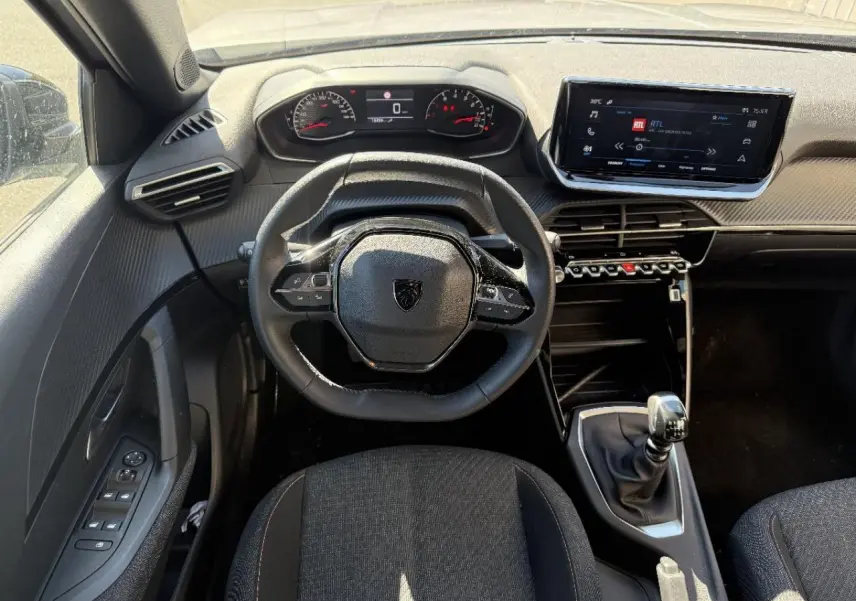 Vue intérieure avant du Peugeot 2008 2025 essence artense, volant compact, tableau de bord numérique et boîte manuelle.