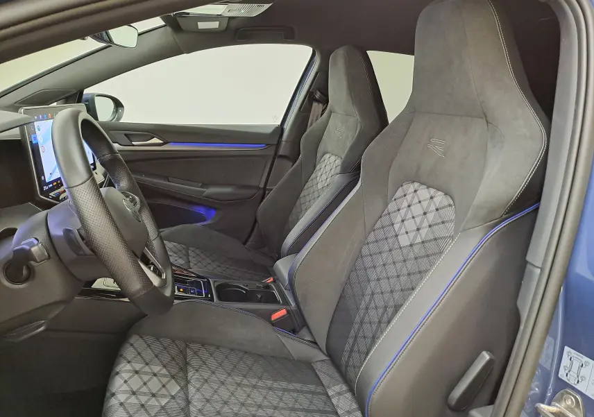 Vue intérieure côté conducteur de la Volkswagen Golf 1.5 eTSI R-Line 2025 avec sièges sport en tissu gris à surpiqûres bleues.