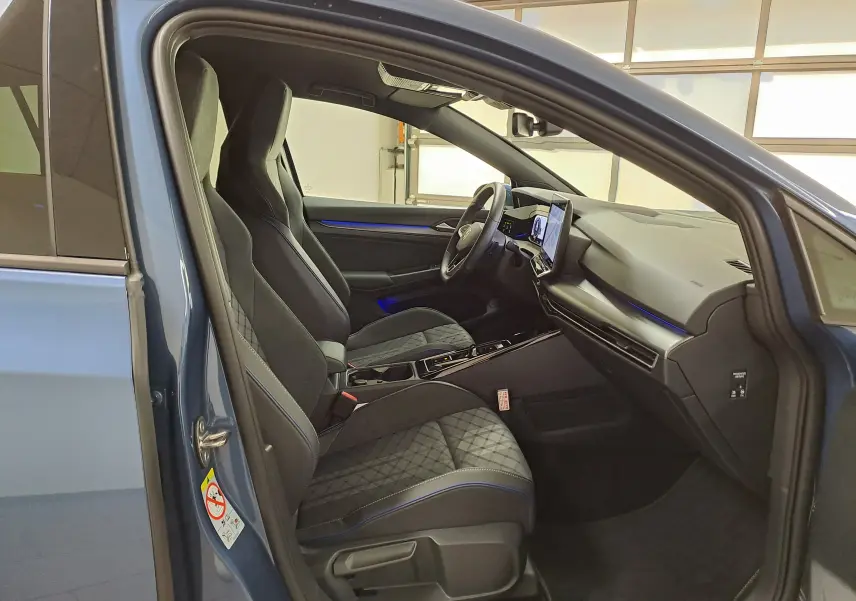 Vue intérieure côté conducteur d'une Volkswagen Golf 1.5 eTSI 150 DSG7 R-Line Edition bleu Anémone avec sièges sport et éclairage d'ambiance bleu.