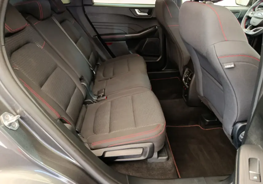 Vue intérieure arrière côté gauche du Ford Kuga 2024 gris clair, sièges tissu noir avec surpiqûres rouges et tapis assortis.