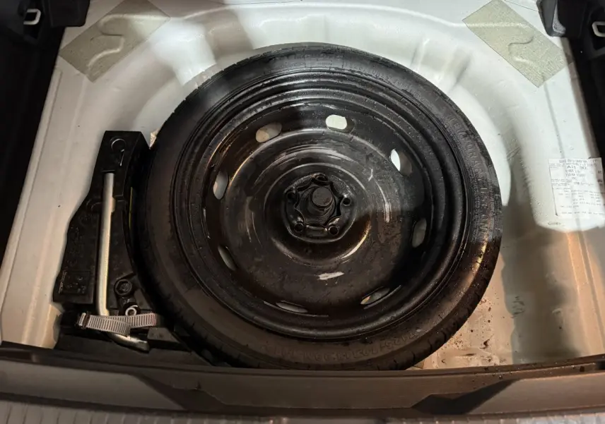 Roue de secours noire dans le coffre blanc d'un Volkswagen T-Roc 2020, avec outils de changement visibles.