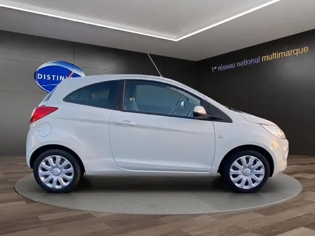 Vue de profil côté gauche d'une Ford KA blanche de 2015, compacte et épurée, sur fond intérieur showroom.