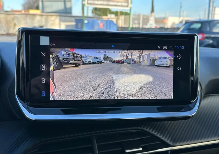 Écran tactile intérieur montrant la caméra de recul d'une Peugeot 208 blanche, vue arrière avec affichage clair.