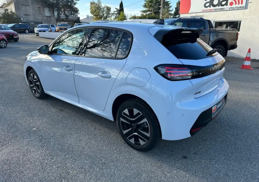 Vue 3/4 arrière droite d'une Peugeot 208 Hybrid 110 blanche avec jantes alliage noires et feux arrière LED distinctifs.