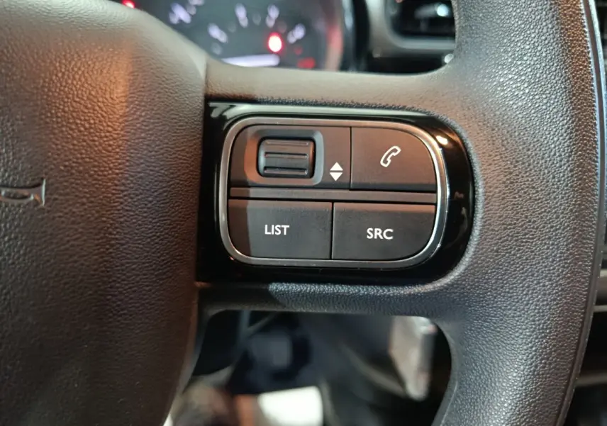 Gros plan sur les commandes gauche du volant noir de la Citroën C3 2024, boutons pour appels et listes multimédia.