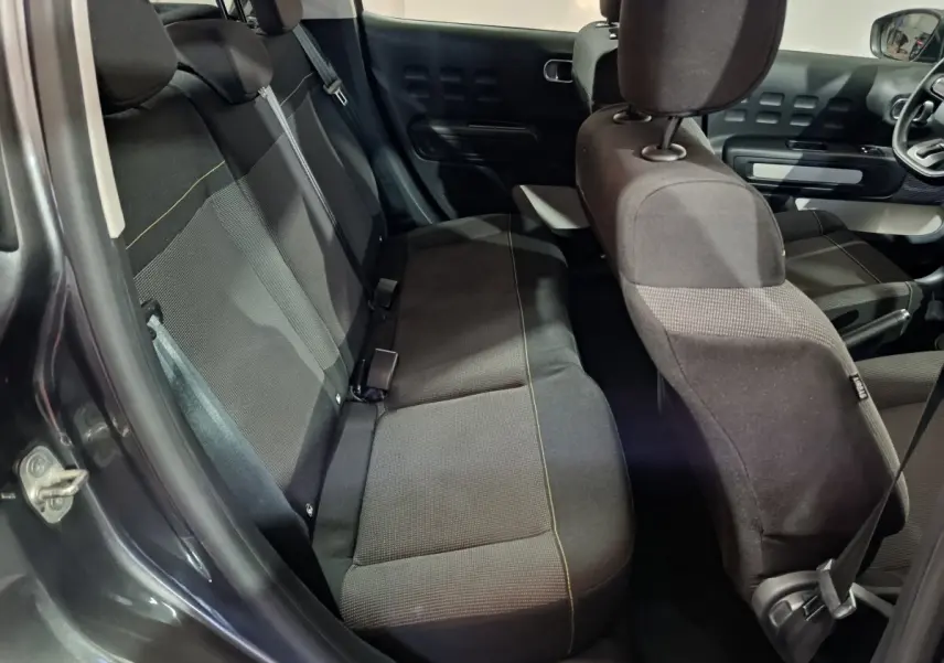 Vue intérieure côté arrière gauche d'une Citroën C3 gris foncé, montrant les sièges tissu et la banquette 3 places.