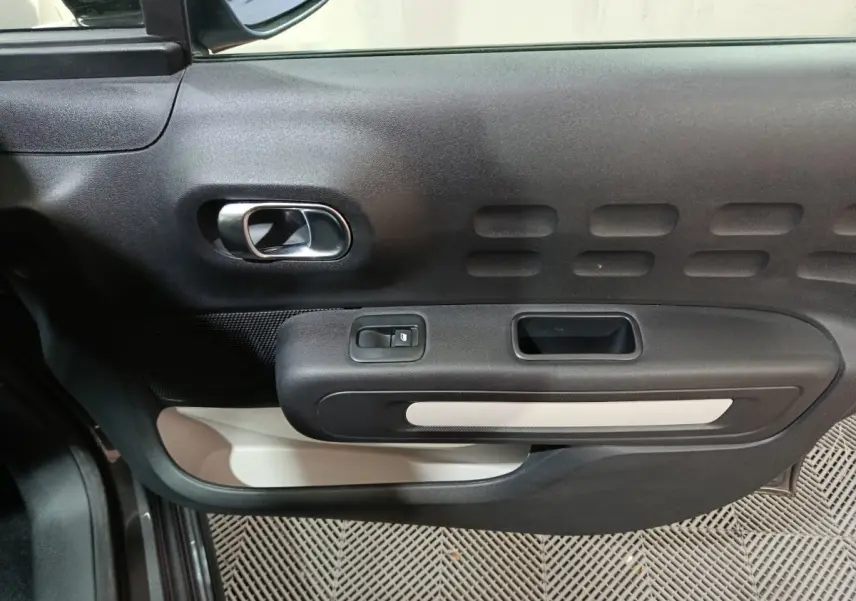 Vue rapprochée de la porte côté conducteur de la Citroën C3 gris foncé, avec poignée intérieure chromée et commandes électriques.