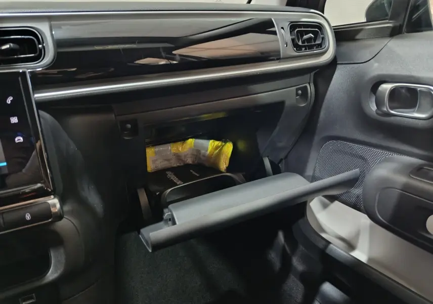 Intérieur de la Citroën C3 gris foncé, vue côté passager avec boîte à gants ouverte et tableau de bord moderne.