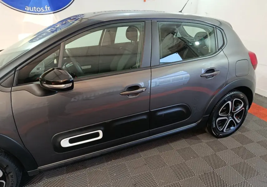 Vue de profil côté gauche d'une Citroën C3 gris foncé avec protections de porte noires et jantes stylisées.