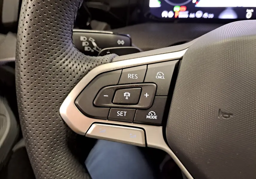 Gros plan sur les commandes du volant à gauche de la Volkswagen Golf 1.5 eHybrid 2025, cuir perforé noir et boutons de régulateur.