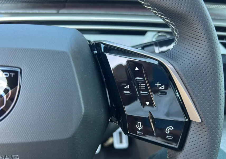Gros plan sur les commandes à droite du volant perforé du Peugeot 3008 Hybrid 2025 gris titane avec logo lion.