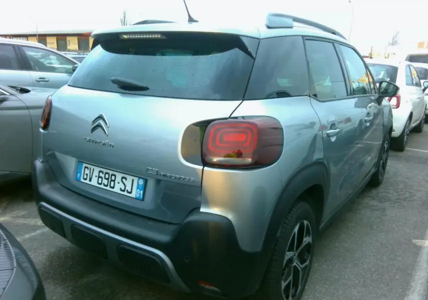 Vue 3/4 arrière droite d'une Citroën C3 Aircross gris foncé avec jantes alliage et barres de toit noires.