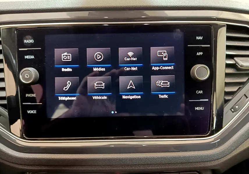 Écran tactile central du tableau de bord du Volkswagen T-Roc blanc, affichant les options multimédias et navigation.