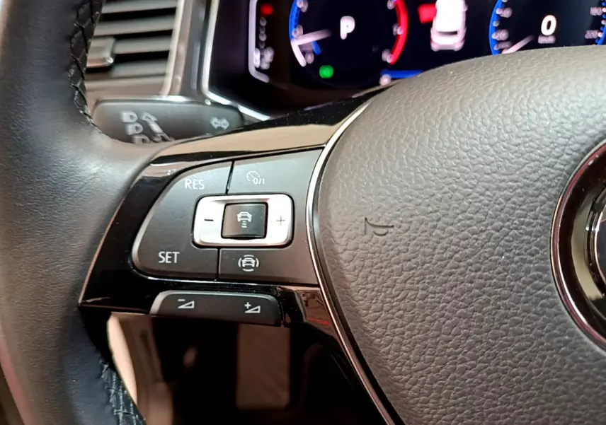 Gros plan sur le volant cuir noir du Volkswagen T-Roc 2020, montrant les commandes de régulateur adaptatif et l'instrumentation numérique bleue.