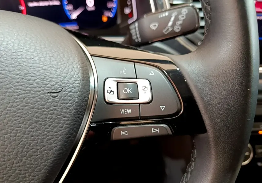 Gros plan sur les commandes multifonctions à droite du volant cuir du Volkswagen T-Roc blanc, tableau de bord numérique en arrière-plan.