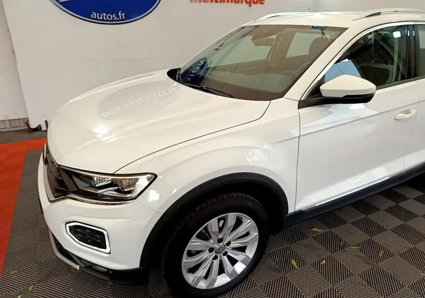 Vue 3/4 avant droit d'un Volkswagen T-Roc blanc avec phares LED et jantes alliage en intérieur showroom.