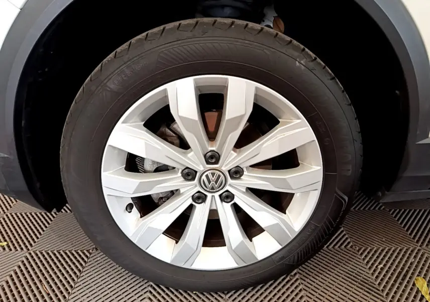 Gros plan sur la roue avant gauche du Volkswagen T-Roc blanc, mettant en valeur la jante alliage à 10 branches et le logo VW central.