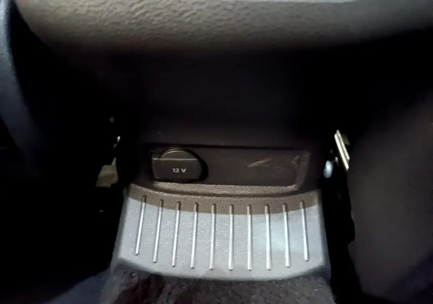 Prise 12V noire en gros plan sous la console centrale du Volkswagen T-Roc blanc, intérieur sombre.