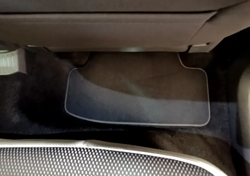 Vue du sol côté passager avant du Volkswagen T-Roc blanc, avec tapis de sol et partie inférieure du siège visible.