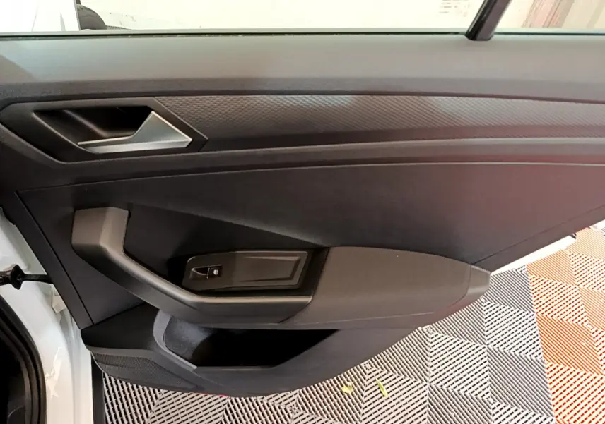 Vue intérieure du panneau de porte côté gauche d'un Volkswagen T-Roc blanc, avec poignée et commande de fenêtre noire.