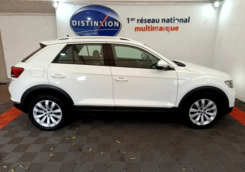 Volkswagen T-Roc blanc en profil côté gauche, stationné en intérieur sur sol damier noir et rouge.