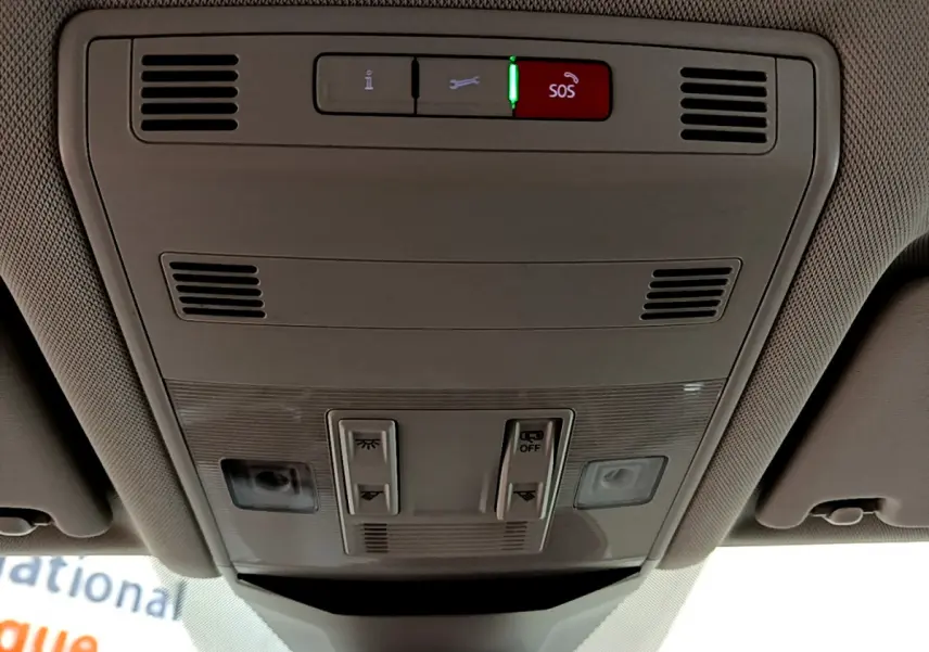 Vue en contre-plongée du panneau de commandes au plafond intérieur du Volkswagen T-Roc blanc, avec bouton SOS rouge allumé.