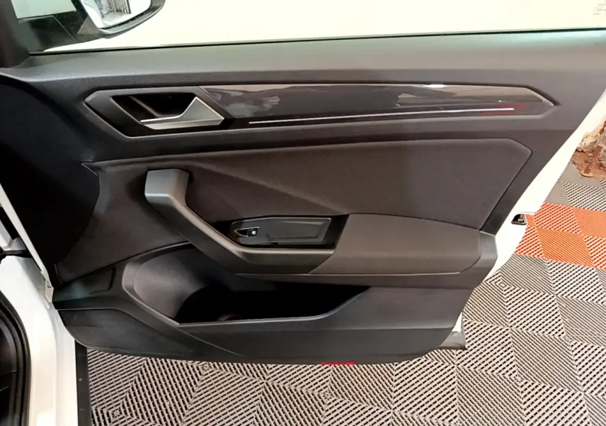 Vue rapprochée de la porte avant gauche noire du Volkswagen T-Roc blanc, avec poignée et panneau de commande.