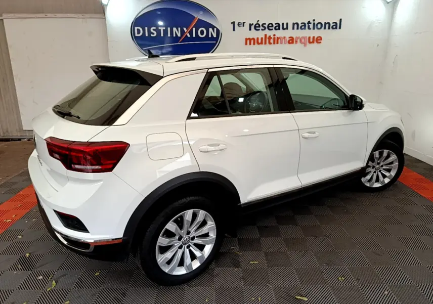 Volkswagen T-Roc blanc vue 3/4 arrière droit en intérieur, avec jantes alliage et toit ouvrant noir.